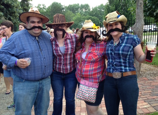 four people wearing fake mustaches at an outdoor event